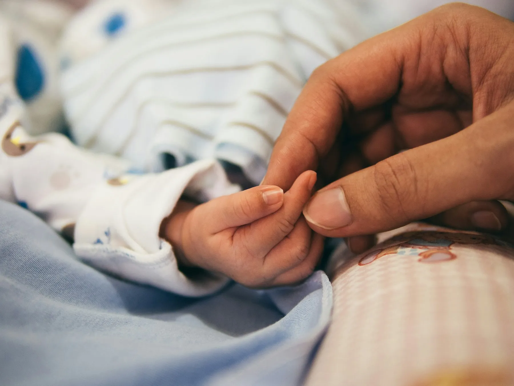 A newborn baby holding an adult finger