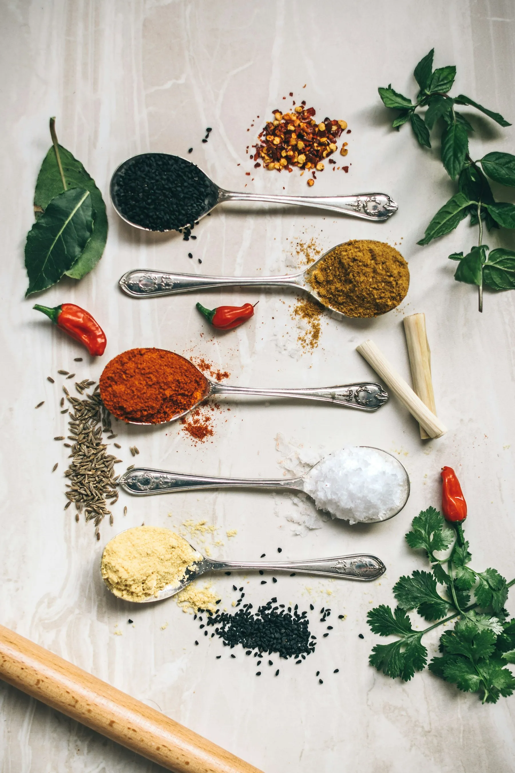 Spoons of ground spices and herbs laid out on a table
